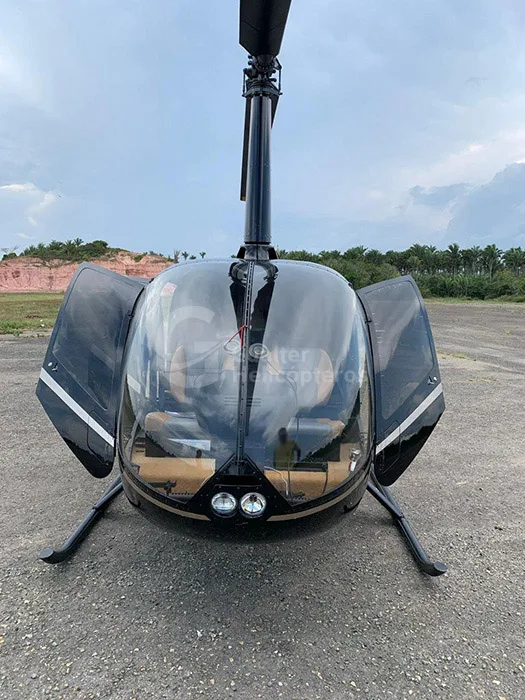 A black Robinson R66 Turbine helicopter with its doors open is parked on an airfield under a cloudy sky.