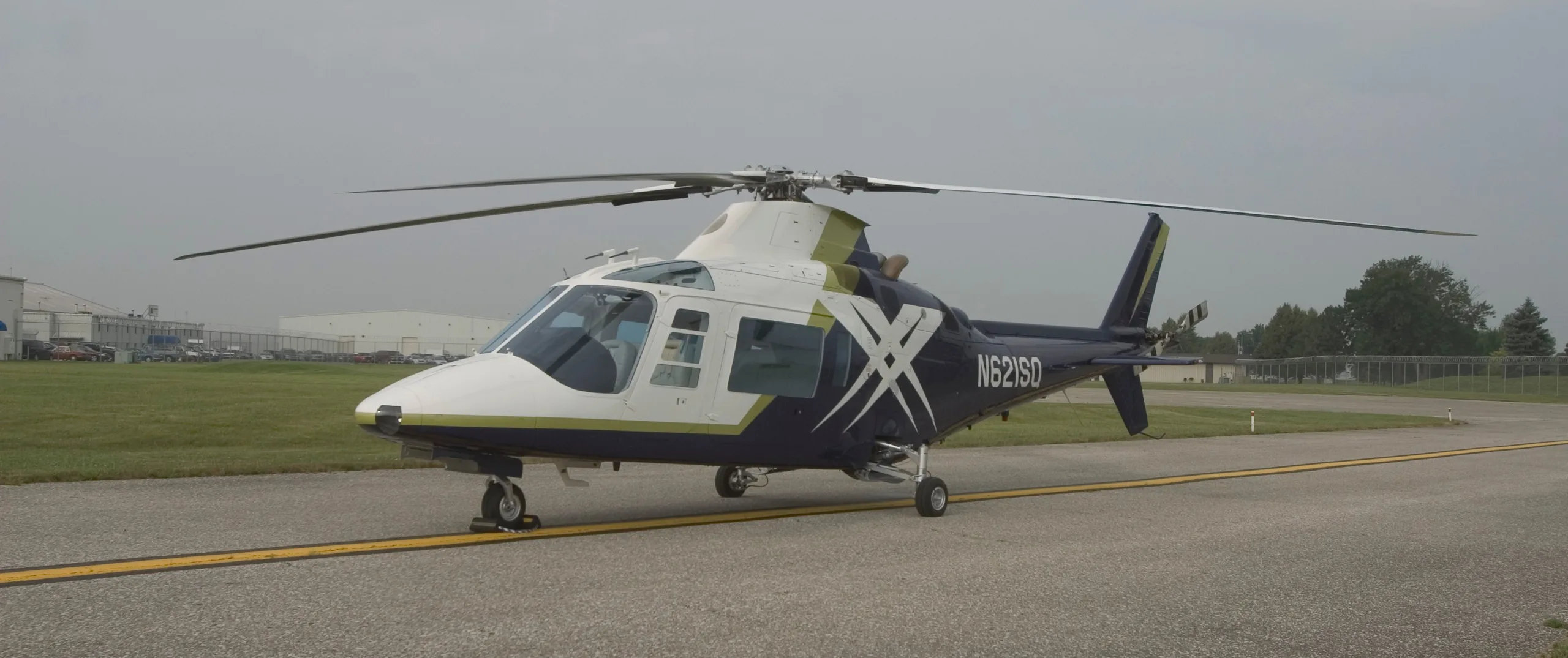 A white and dark blue helicopter with a green stripe and N621SD tail number parked on an airfield.