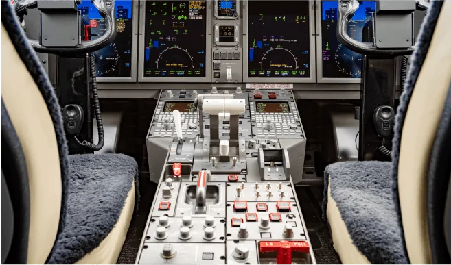 The cockpit of a modern private jet displays multiple digital screens, control yokes, and a central throttle quadrant.