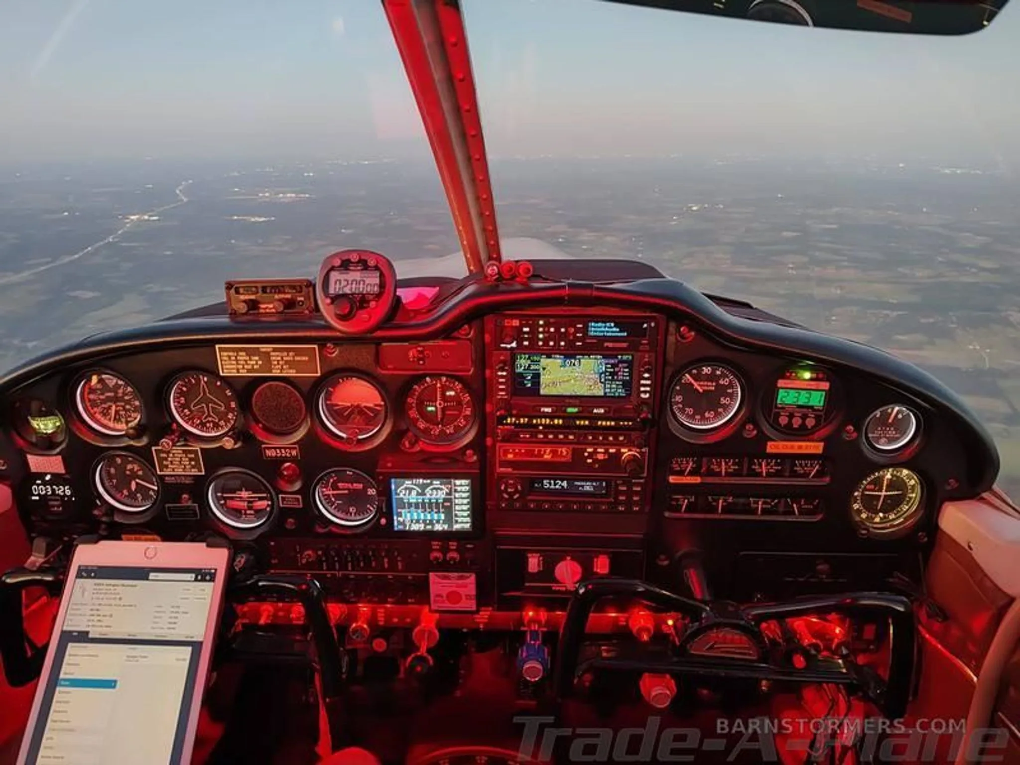 The illuminated cockpit of a Piper Cherokee 235 at night, showing the instrument panel and controls with city lights below.