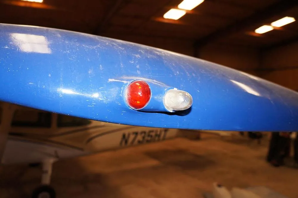 A close-up view of the red and white navigation lights on the blue wingtip of Cessna N735HT.