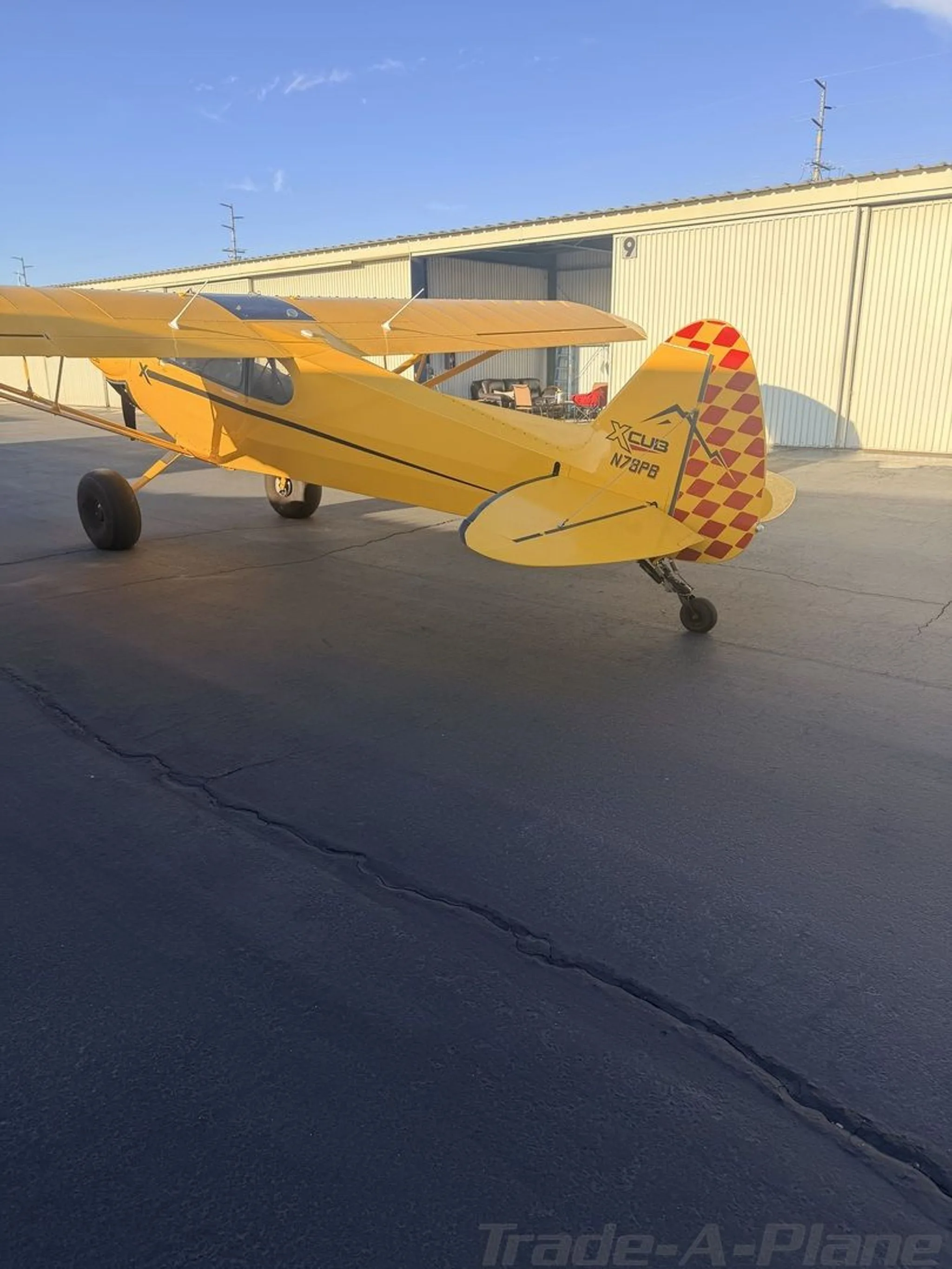 A rear view of the yellow CubCrafters XCub N78PB, showing its red and white checkered tail, parked on an asphalt tarmac.