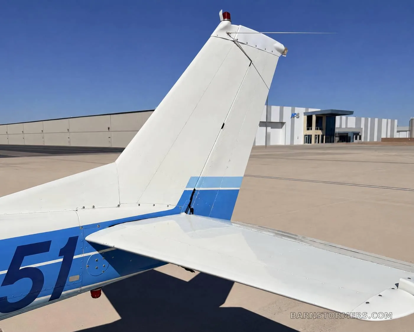 A close-up view of the white and blue tail section of a single-engine propeller aircraft, showing part of the tail number.