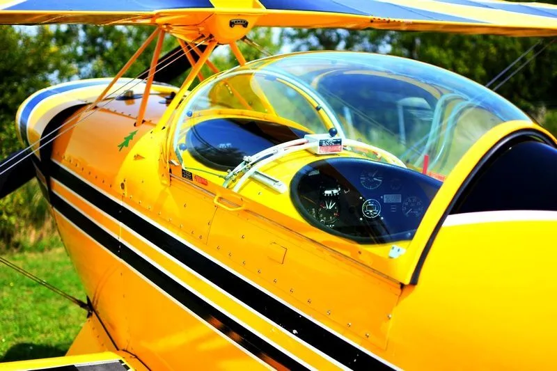 A yellow biplane with black stripes and a clear canopy, viewed from the side on a grassy field.