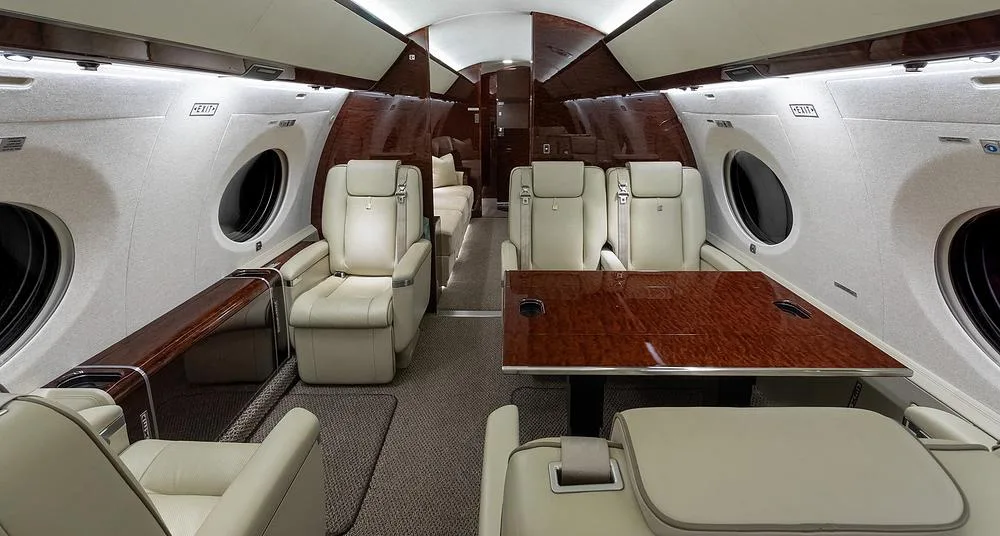 A view of the Gulfstream G650's cabin interior featuring light leather seats, a polished wood table, and dark wood paneling.