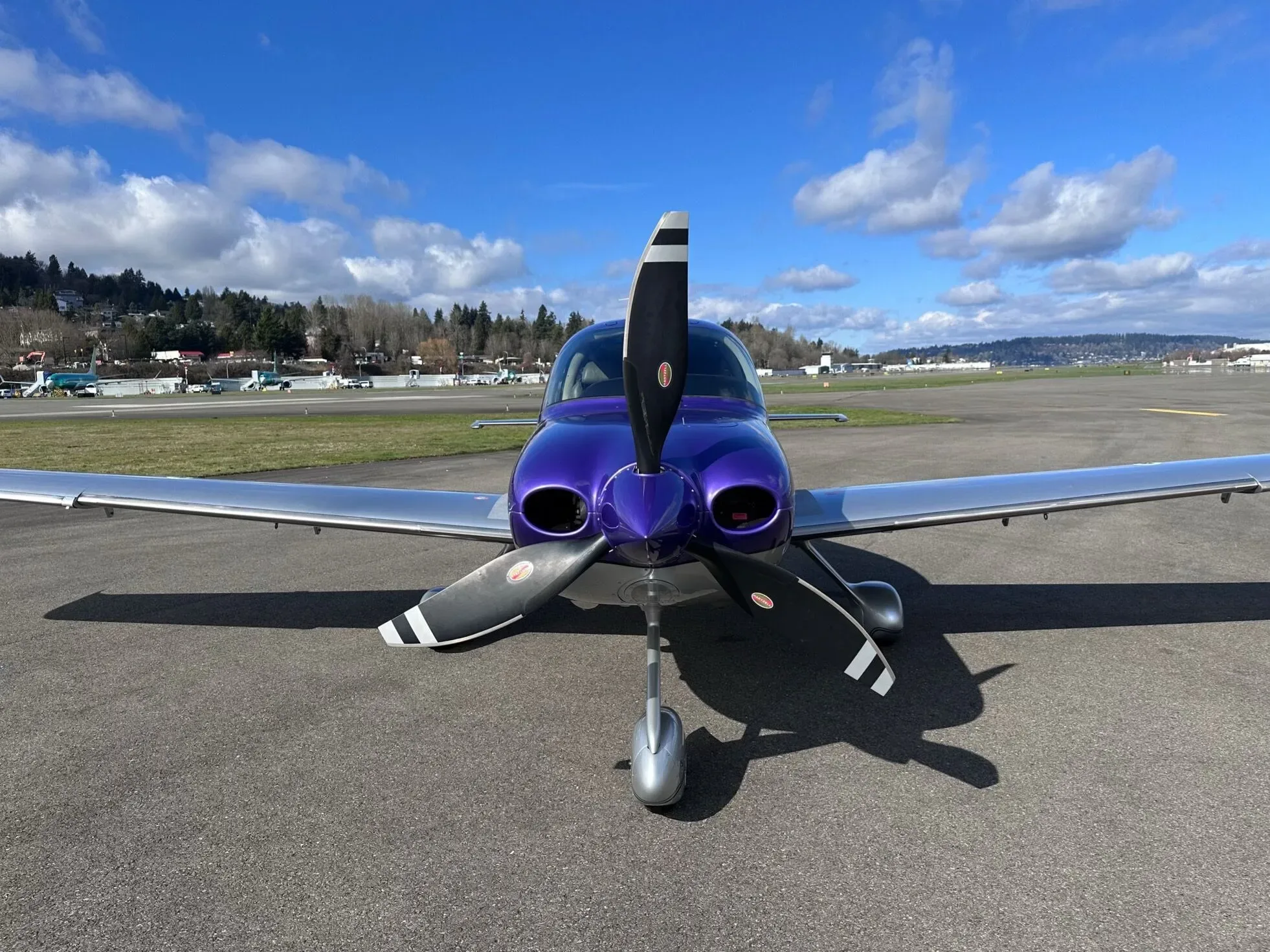 A head-on view of the purple and silver Cirrus SR22 aircraft, N380BW, with its propeller centered on an airport runway.