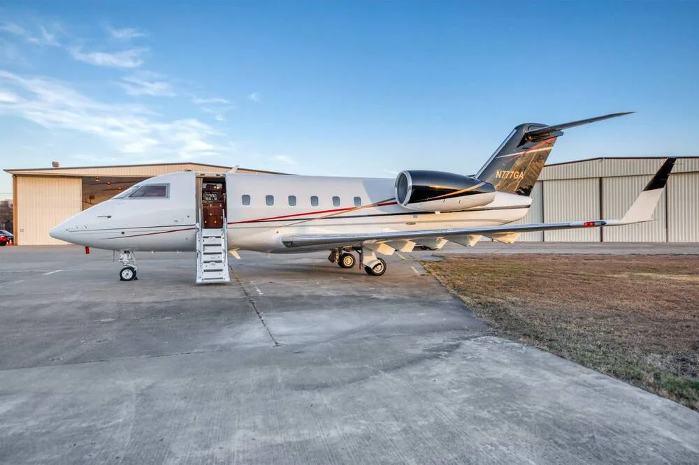 A white business jet with a dark brown and red tail, registration N777GA, parked on an airfield with its main door open and stairs extended.