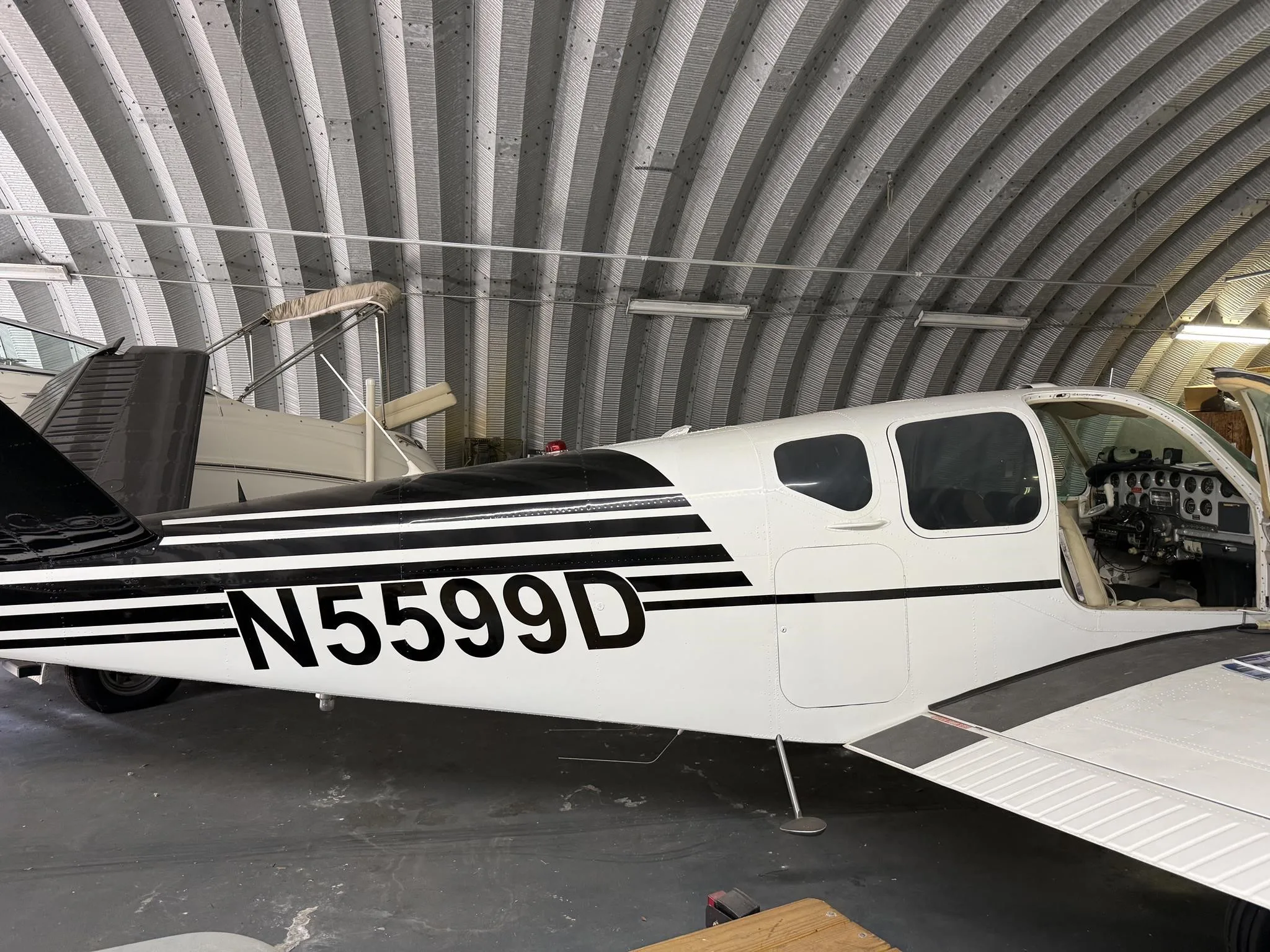 A white single-engine aircraft with black stripes and registration N5599D, parked inside a hangar.