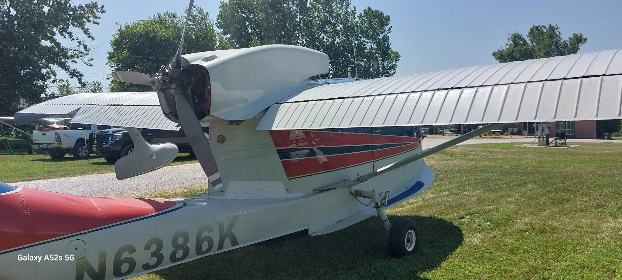 A close-up view of the engine, wing, and tail of the N6386K amphibious aircraft on a grassy field.