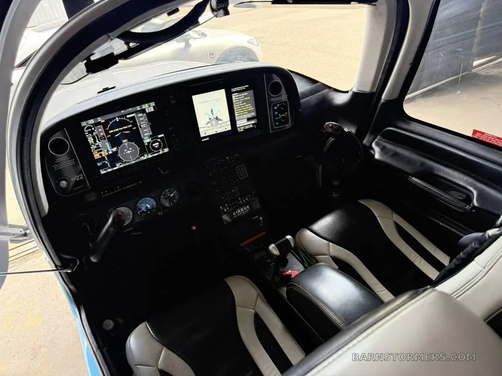 The cockpit of a Cirrus SR22 aircraft, showing the instrument panel with multiple screens and black and white leather seats.