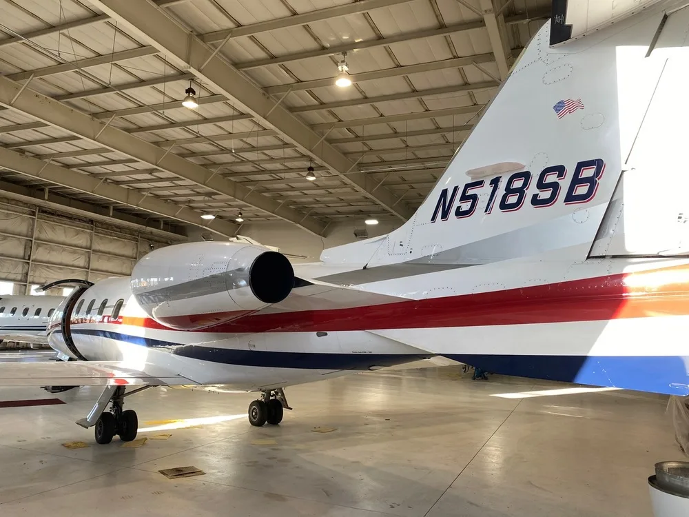 The tail section of a white business jet with red and blue stripes, registration N518SB, inside a hangar.