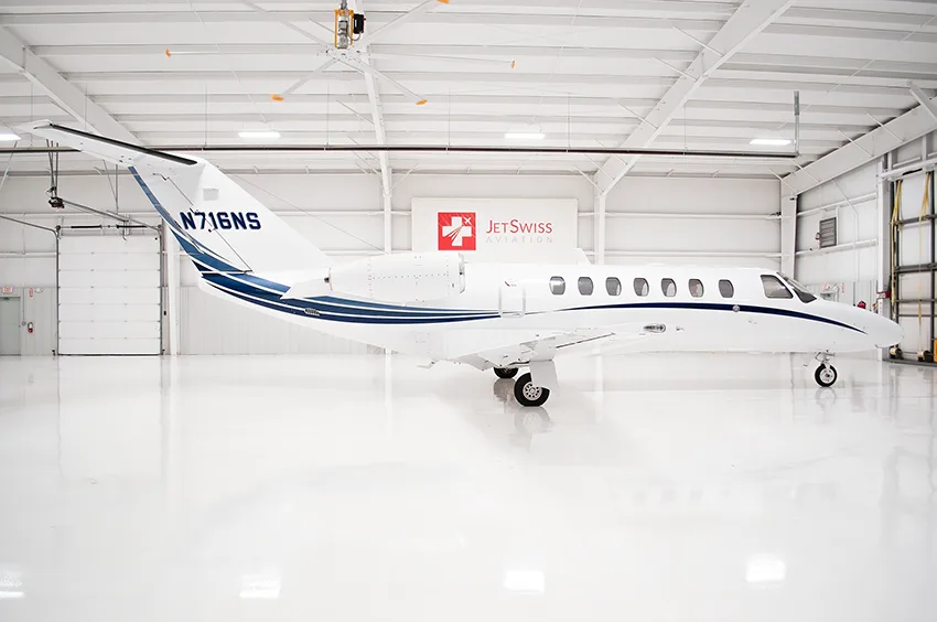 A white business jet with blue stripes (N716NS) seen from the side in a hangar.