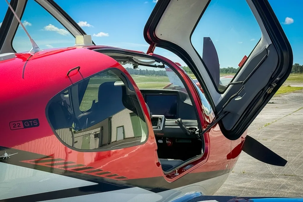 A close-up of the red and silver Cirrus SR22 GTS with its gull-wing doors open, revealing the cockpit.