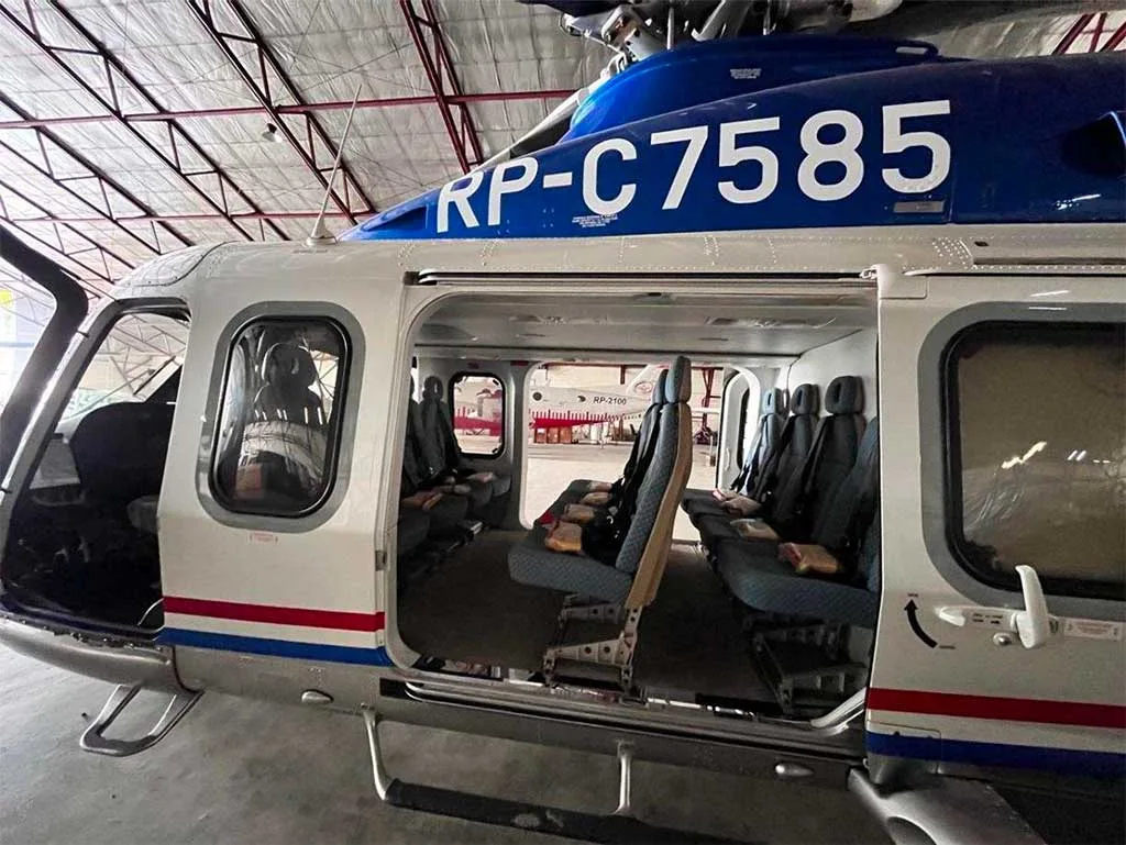 A blue and white helicopter, registration RP-C7585, with its side door open, parked inside a hangar.