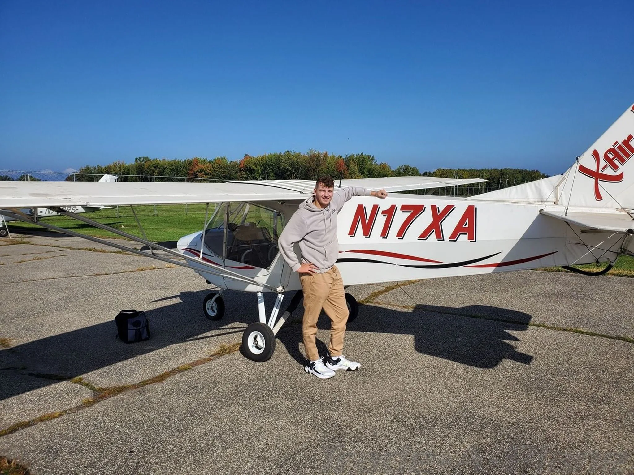 A man stands next to a white X-Air aircraft with red and black stripes, registration N17XA, on an airfield.