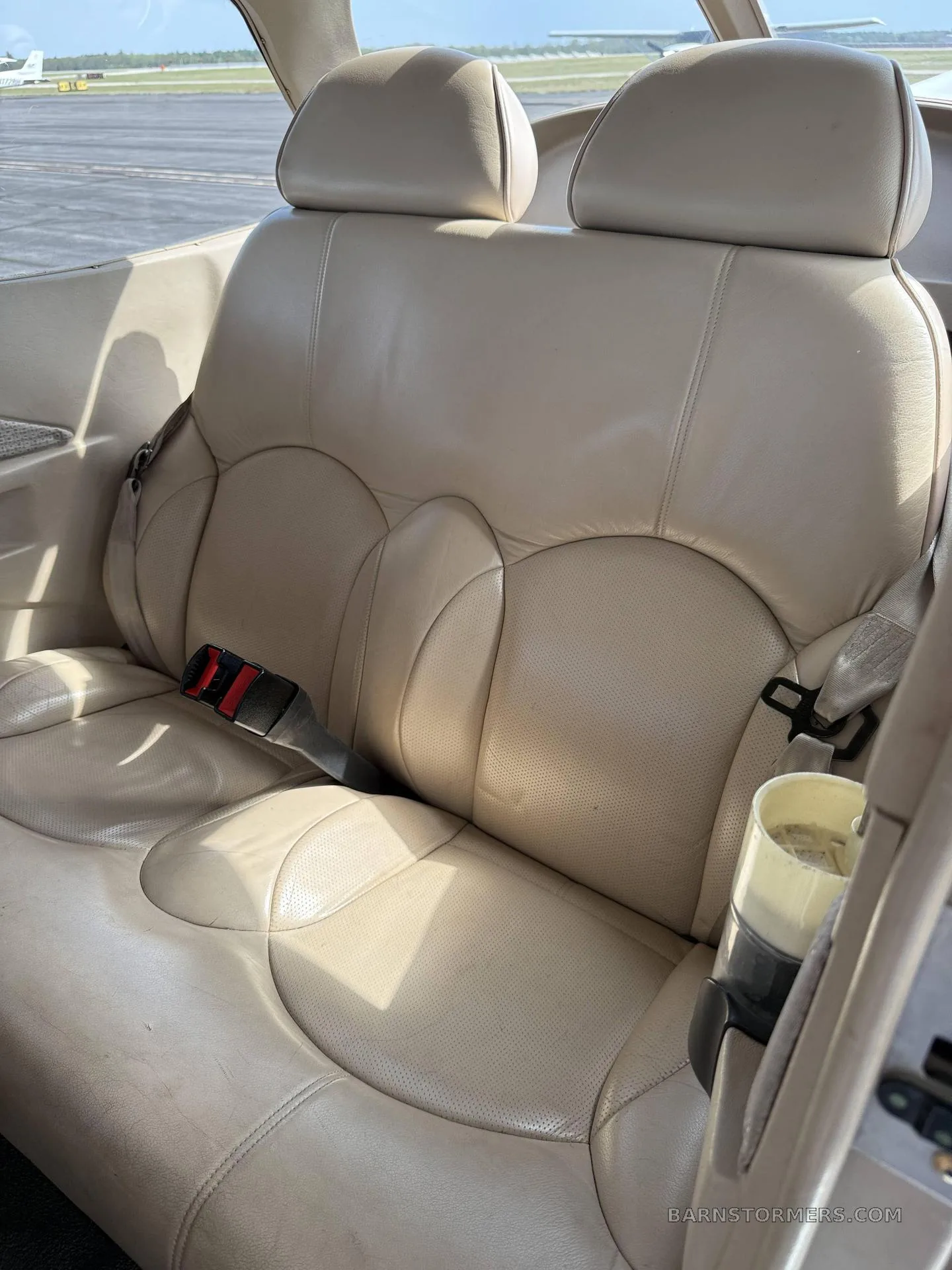 The beige leather rear seats of a small aircraft cabin, with seatbelts visible.
