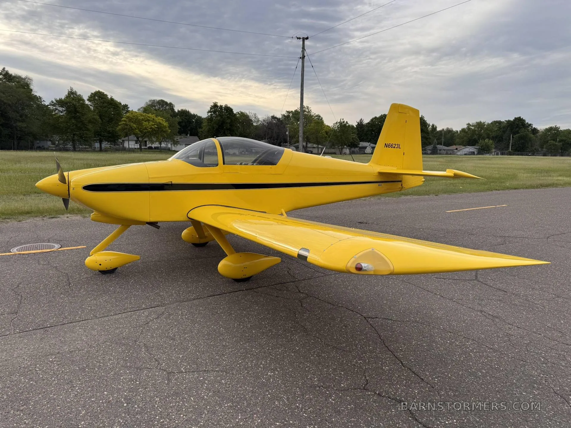 A bright yellow single-engine aircraft with a black stripe and registration N6623L is parked on an asphalt ramp under a cloudy sky.