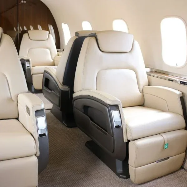 Angled view of two beige leather aircraft seats with dark accents in a private jet cabin.