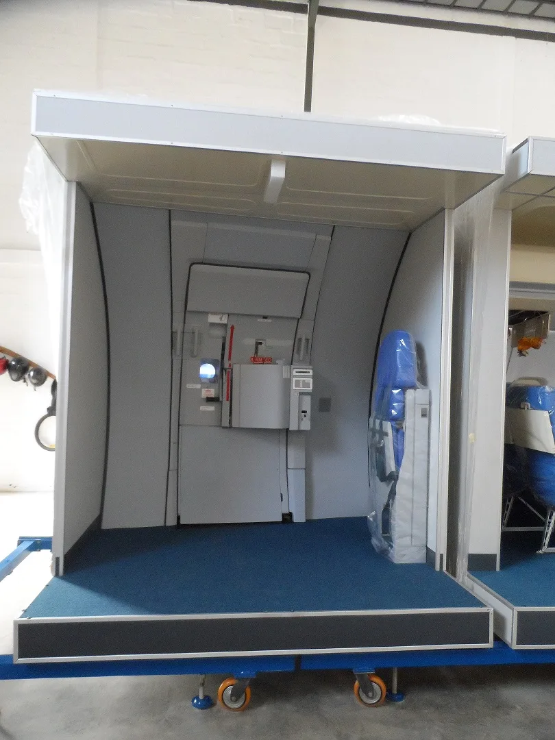 A training mock-up section showing an aircraft cabin door and blue carpet.