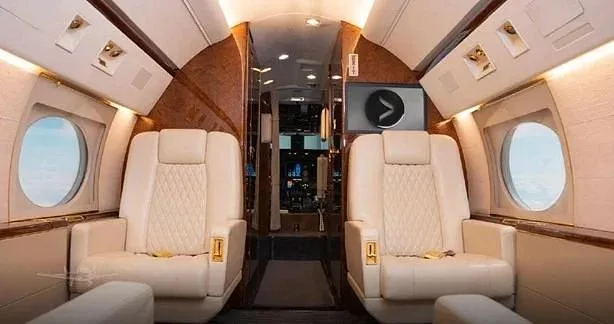 The luxurious interior of a business jet cabin features two cream-colored quilted leather seats facing forward.