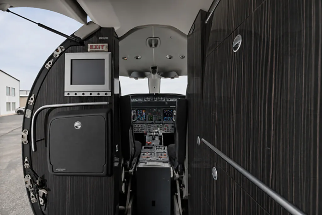 The entry area of a private jet, looking forward into the cockpit with its illuminated instrument panel.