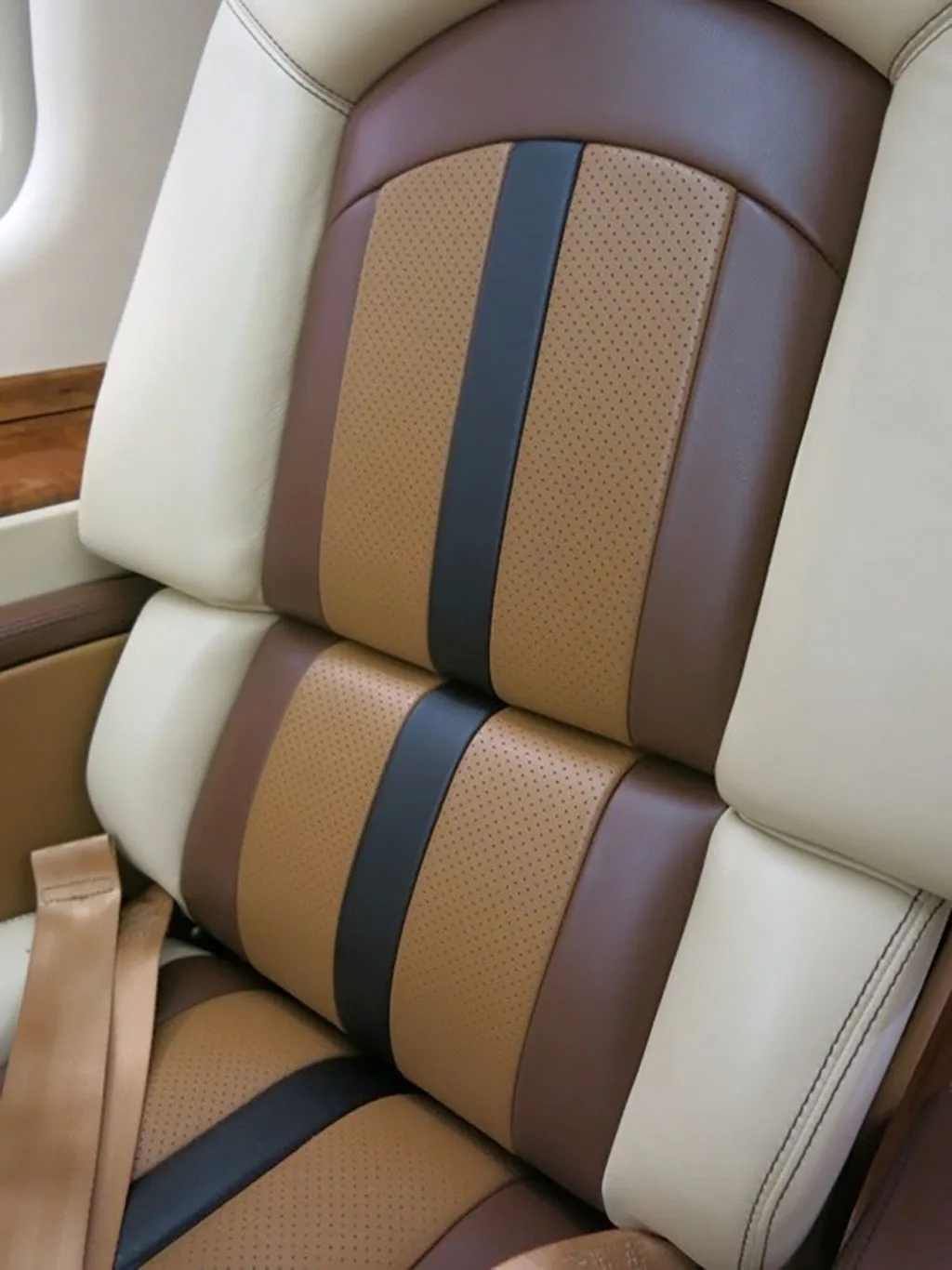 A close-up view of a beige, brown, and black striped leather aircraft seat with perforated details.