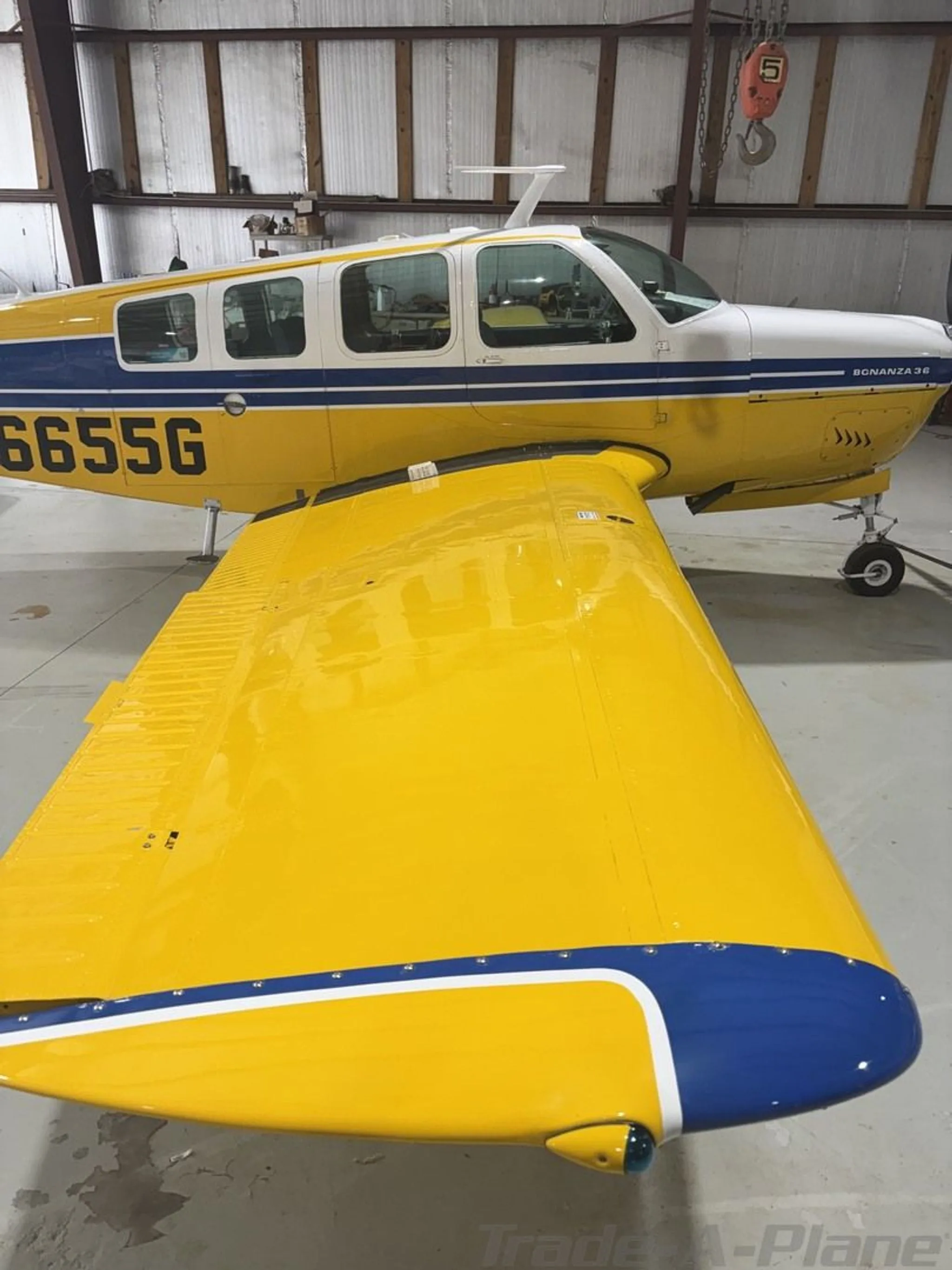 Side view of a yellow and white Beechcraft Bonanza 36 with registration N6655G, parked in a hangar.