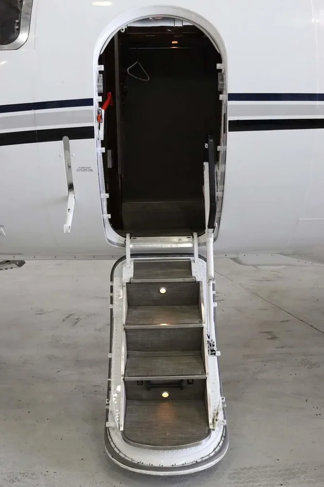 The open main entry door of the business jet with illuminated integrated airstairs extended.