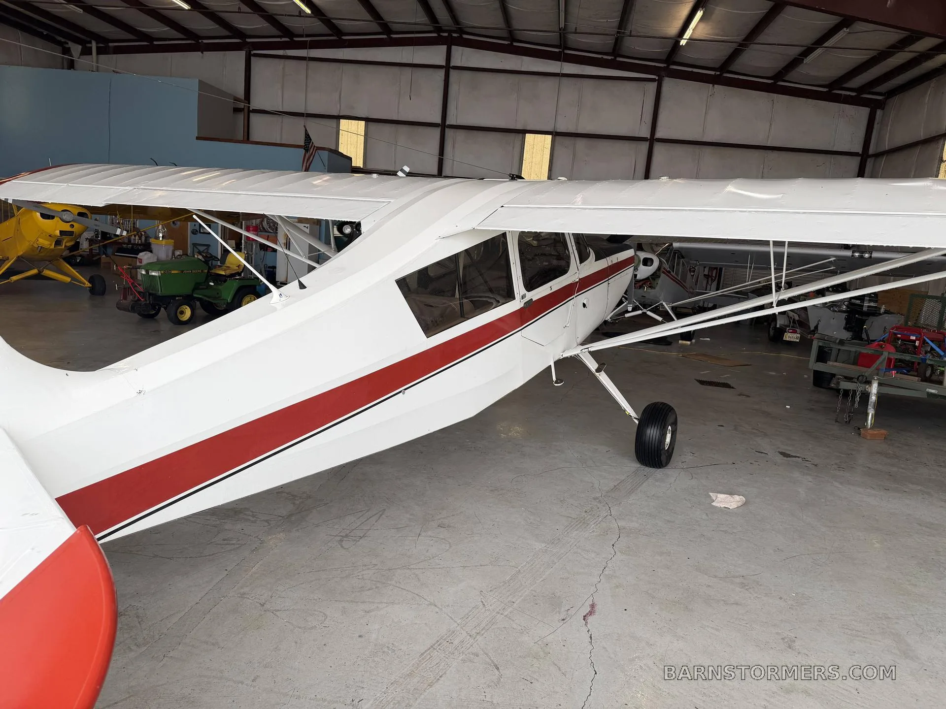 A side view of a white and red high-wing aircraft parked in a hangar, with other equipment in the background.