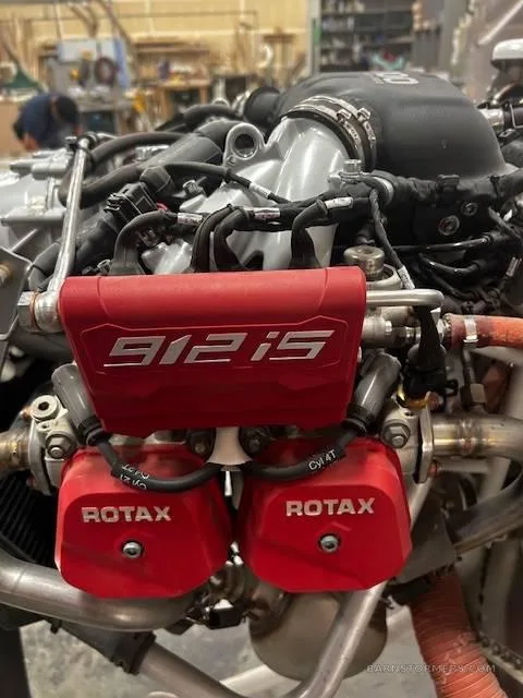 Close-up view of a Rotax 912iS aircraft engine with red covers, showing detailed components.
