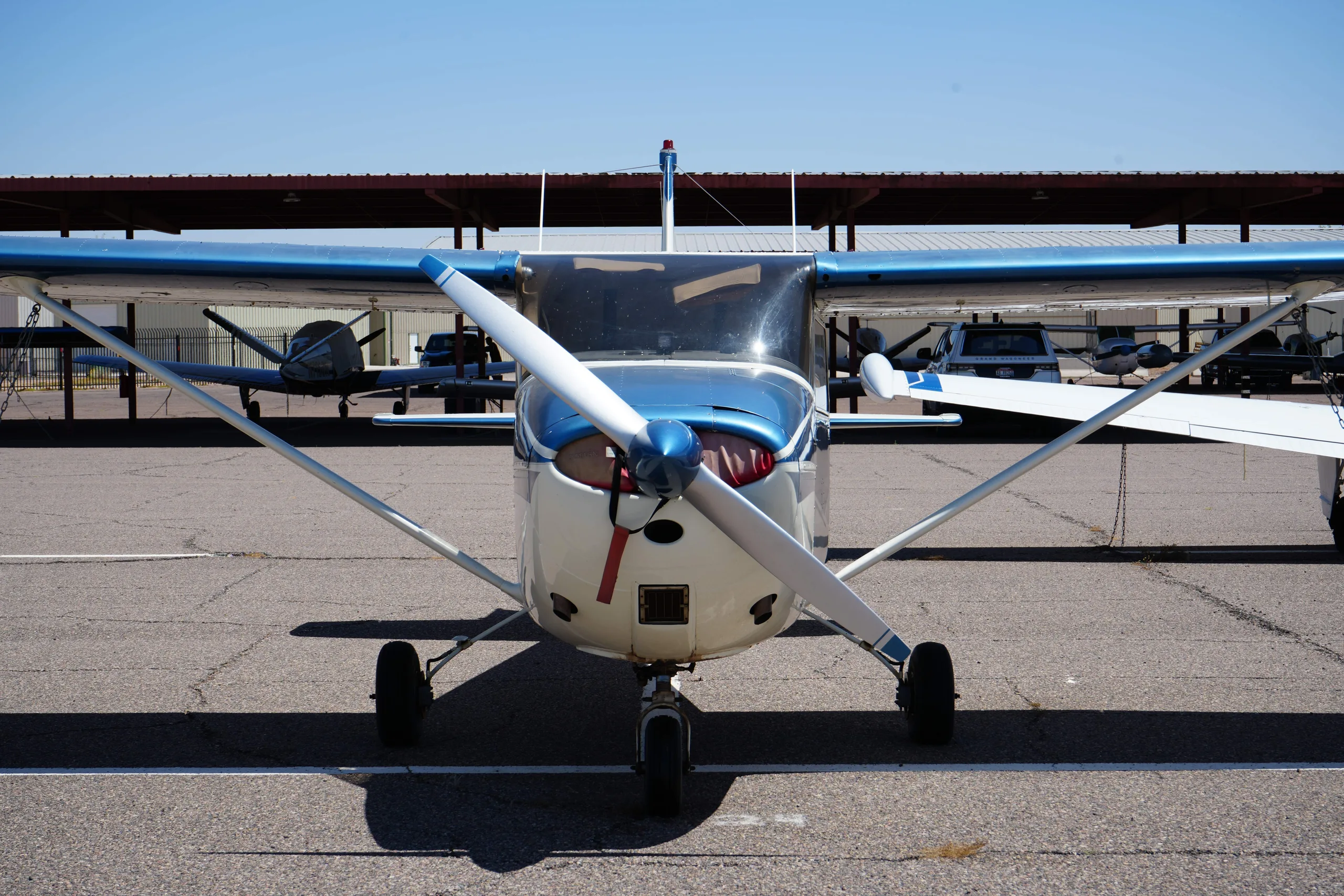 Front view of a white and blue Cessna 172 parked on an airfield under a clear sky.