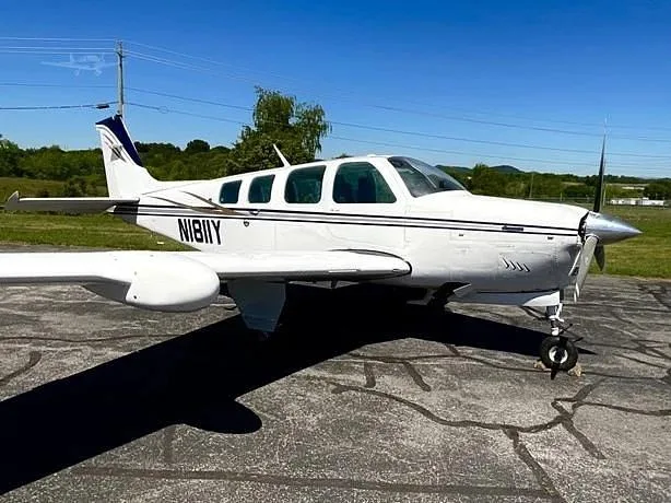 A white single-engine aircraft with dark blue accents, registration N1811Y, parked on an asphalt ramp under a clear sky.