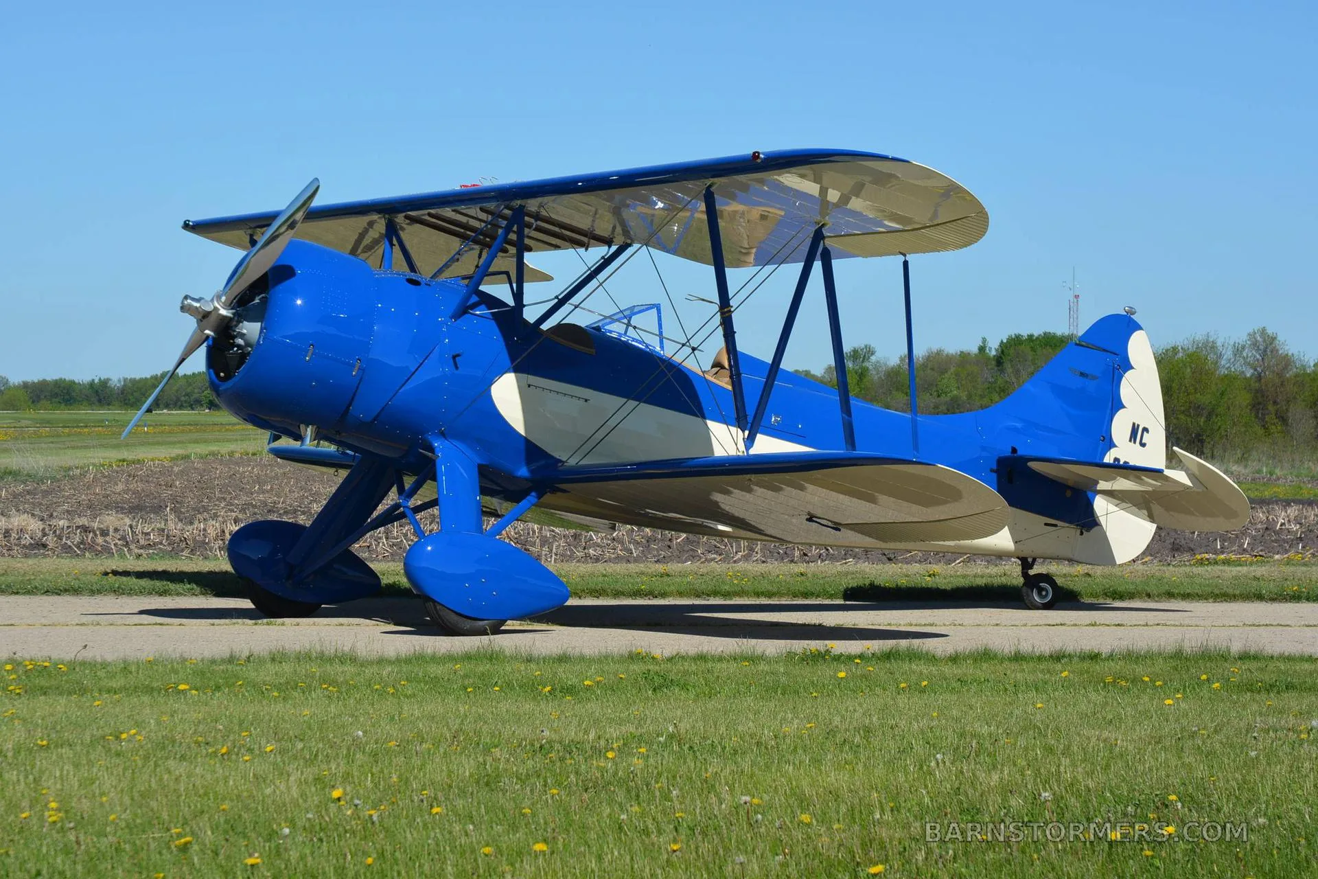 A blue and white biplane with registration N32063 parked on an asphalt runway next to a grassy field.