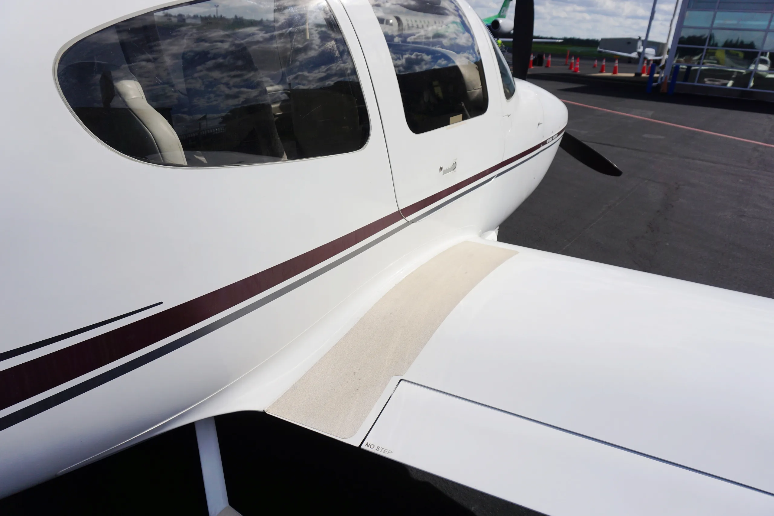 View of the light gray rear cabin seats and ceiling of a Cirrus SR22, looking out to an airport tarmac.