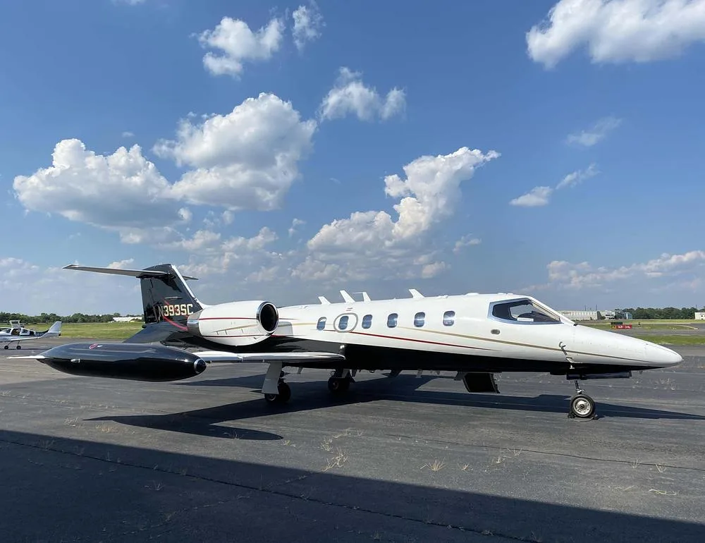 A Learjet 35A with a white fuselage and black tail/nacelles, parked on an asphalt tarmac under a partly cloudy sky.