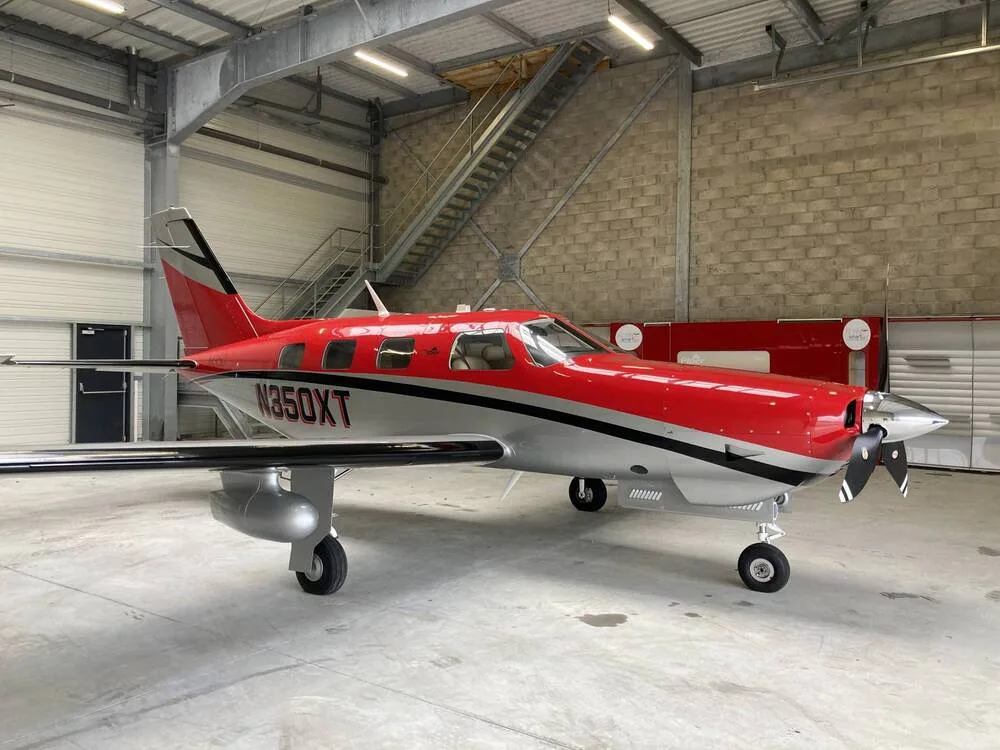 A red and silver Piper M350 aircraft, registration N350XT, parked inside a hangar.