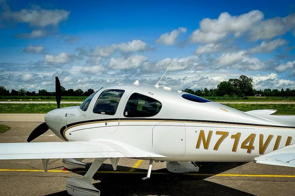 A close-up side view of the white and silver Cirrus SR22 aircraft with gold and black accents, registration N714VU, parked on an airfield.