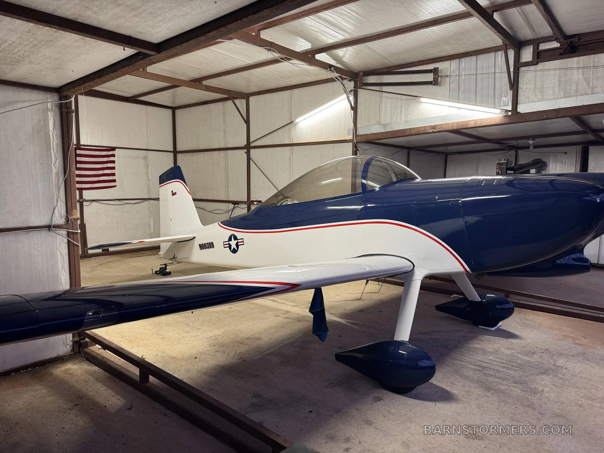 A blue and white single-engine aircraft, registration N663BH, parked inside a hangar, viewed from the front-right.