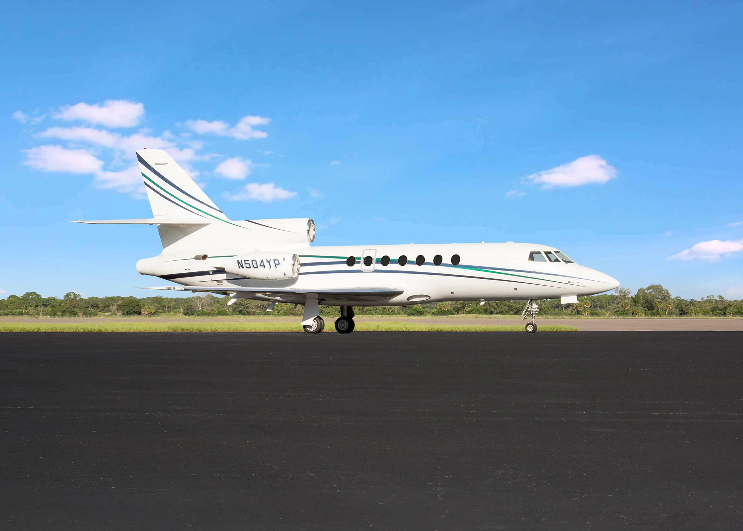 A white business jet with green and blue stripes and registration N504YP parked on a tarmac under a blue sky.