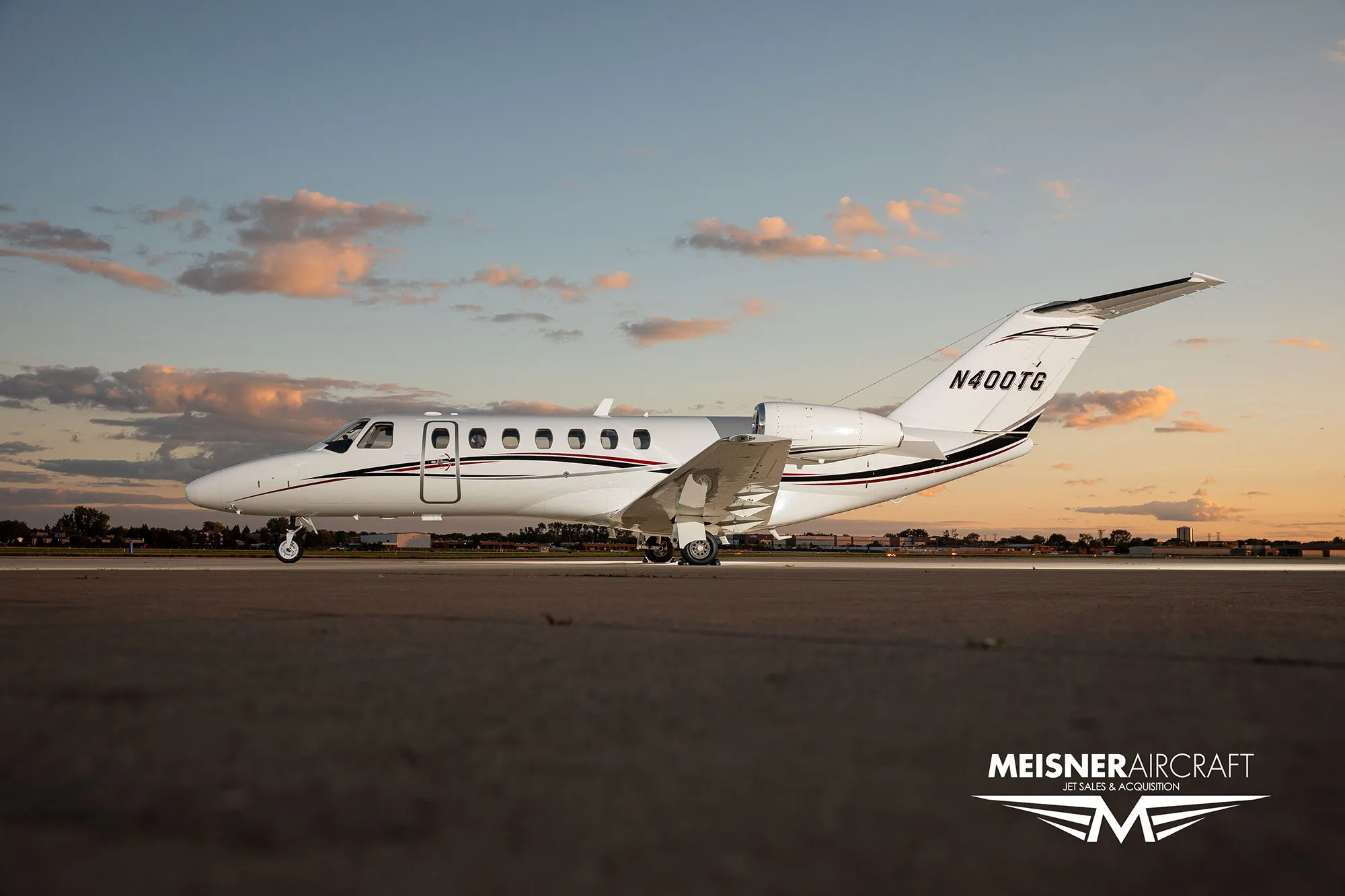 A white business jet with black and red stripes (N400TG) sits on a tarmac at sunset, with a 'Meisner Aircraft' logo.