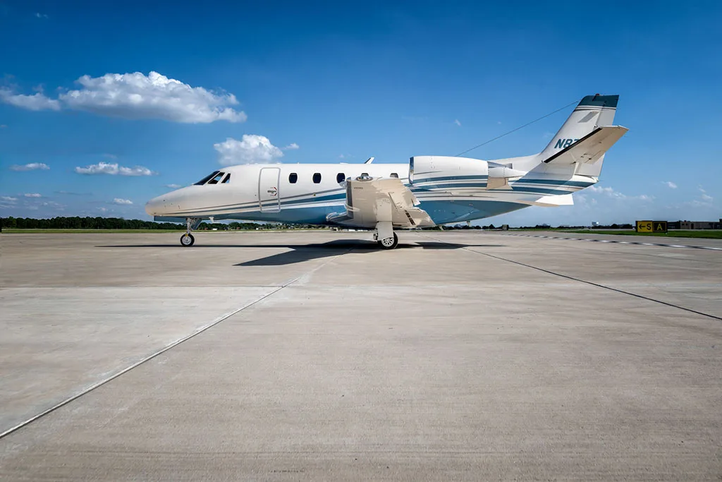 A side view of the Cessna Citation Latitude business jet, N8701L, parked on an airfield under a blue sky.