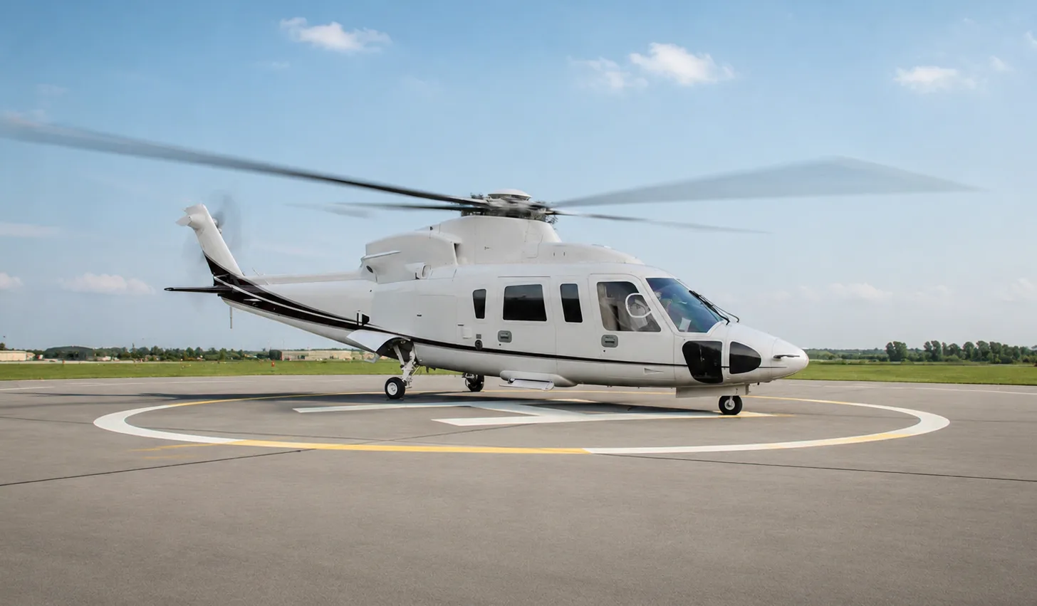 A white executive helicopter with black accents sits on a helipad with its rotors spinning under a blue sky.