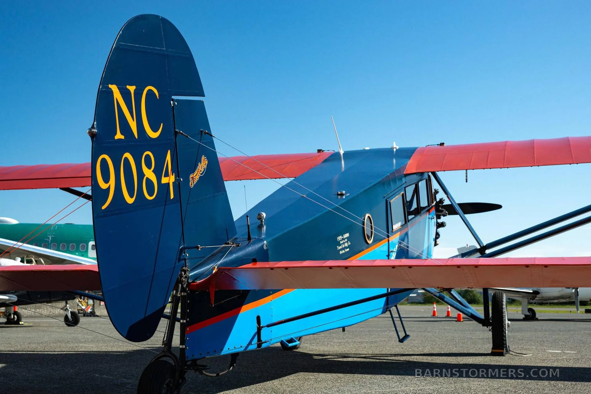 A rear view of a vintage blue and orange aircraft, showing its tail with registration NC 9084 and a partial view of another aircraft.
