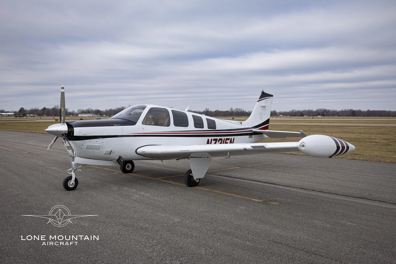 A white and black single-engine propeller aircraft with red stripes, N721EN, parked on an asphalt runway under a cloudy sky.