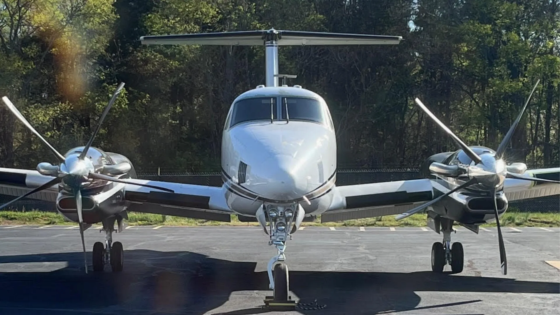 A head-on view of a white and black twin-engine turboprop aircraft, likely a Beechcraft King Air, parked on an asphalt surface.