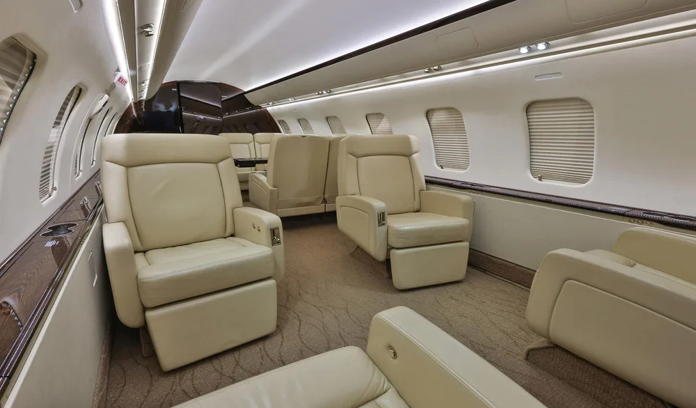 The interior cabin of a private jet, featuring light beige leather seats and a patterned carpet.