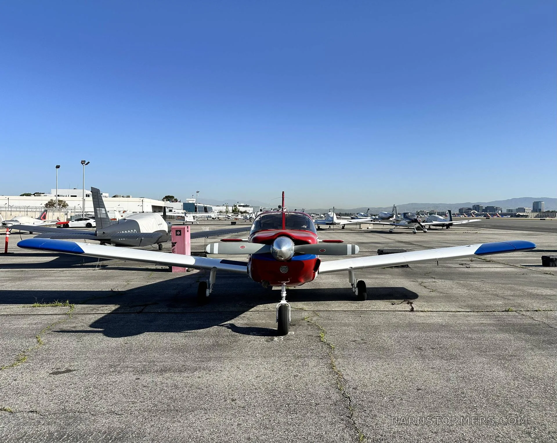 A front view of a red, white, and blue single-engine propeller aircraft (N3011K) parked on an airport ramp.