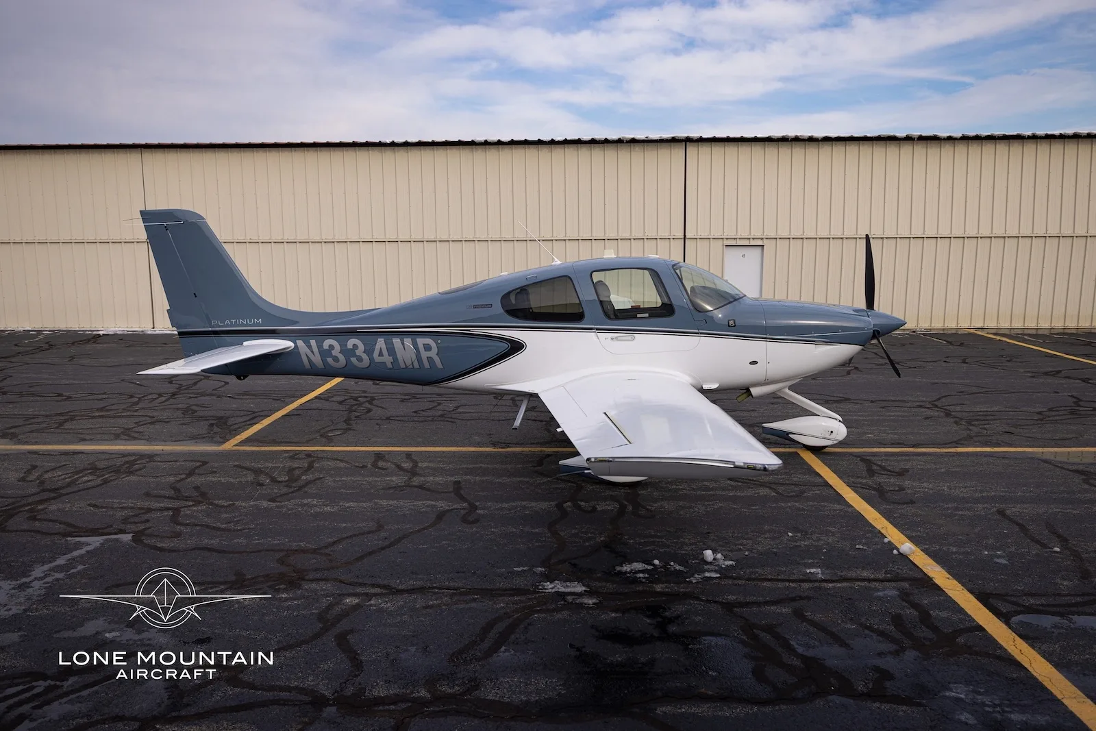 A side view of the Cirrus SR20 aircraft, N334MR, in blue and white, parked on a tarmac.