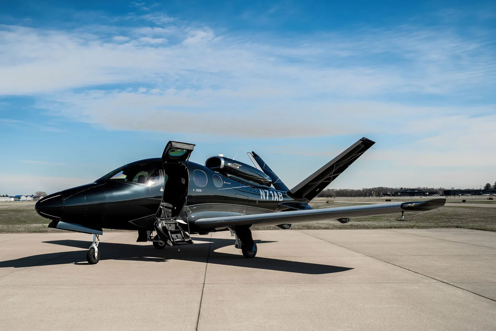 Side view of a black Cirrus Vision Jet (N71AB) parked on an airport tarmac with its main door open.