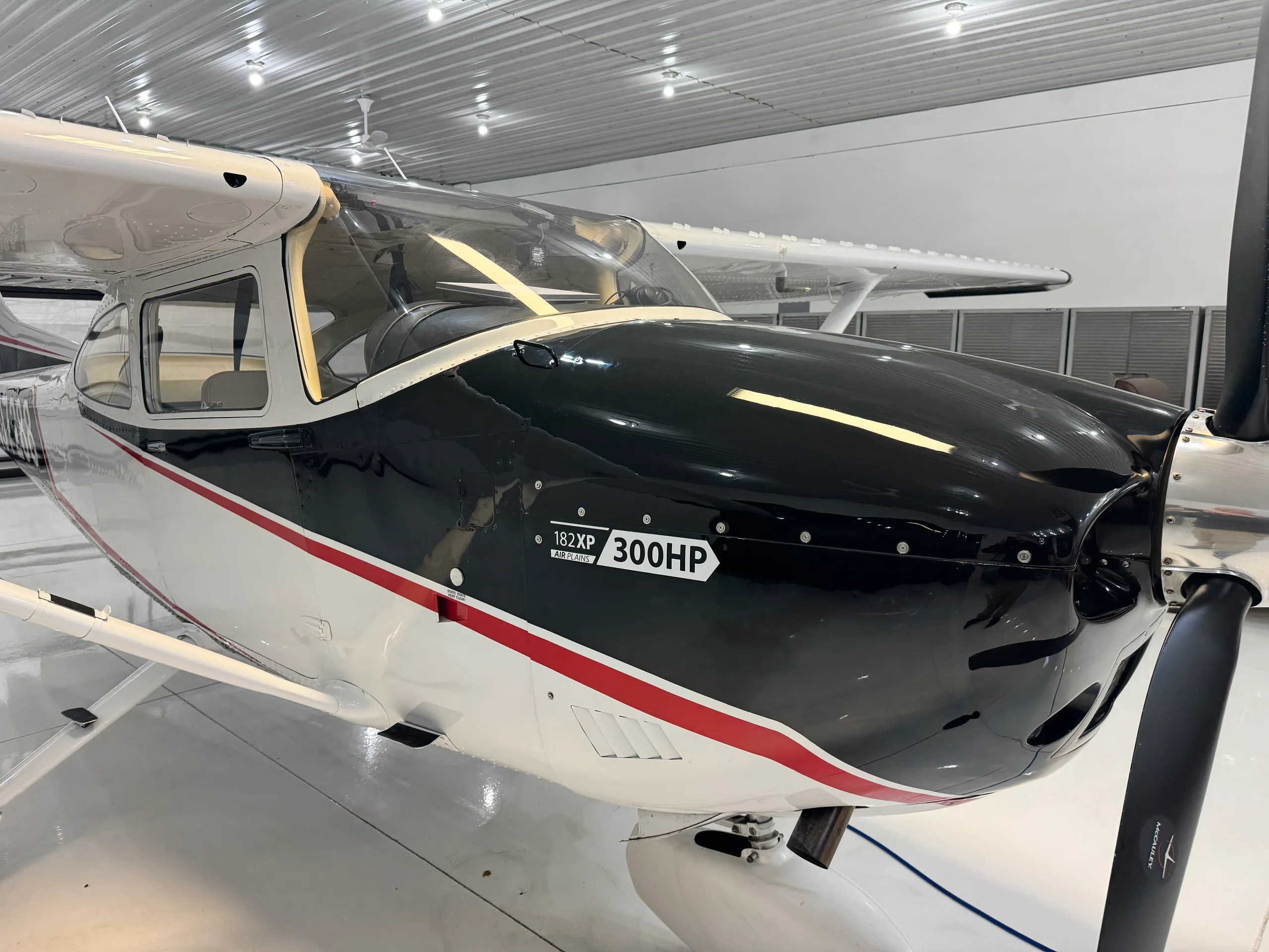 A close-up view of the front-right side of a black and white Cessna 182XP 300HP aircraft in a hangar.